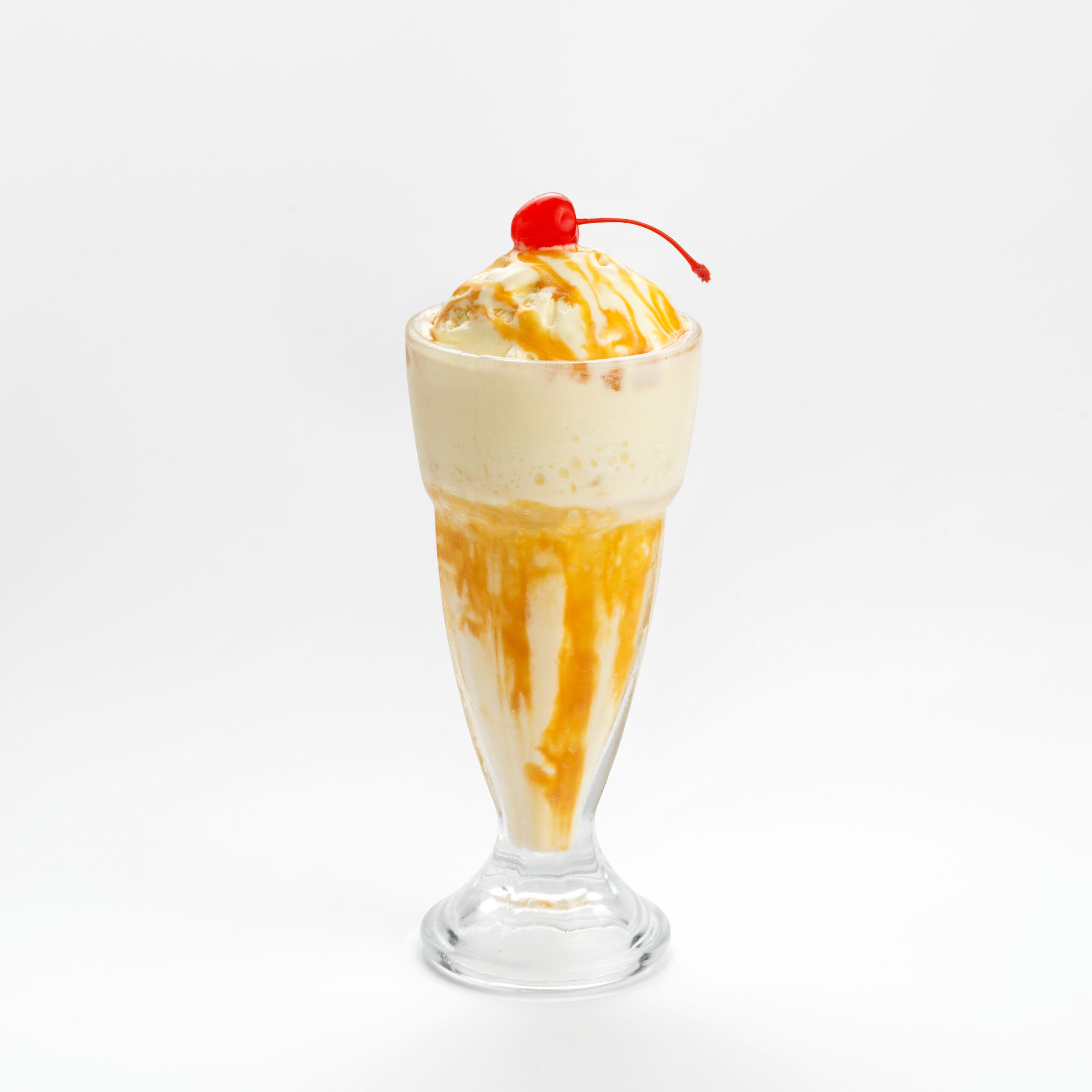 Vanilla milkshake with caramel sauce & cherry on top in a white background